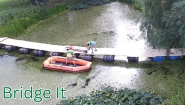 Billedet viser teambuildingaktiviteten Bridge It, hvor deltagerne bygger en flydende bro hen over vand ved hjælp af tønder, brædder og reb. Aktiviteten kræver både samarbejde, kommunikation og praktisk snilde – og giver en sjov udfordring i naturen, hvor hele teamet skal arbejde sammen for at skabe en stabil forbindelse over vandet.