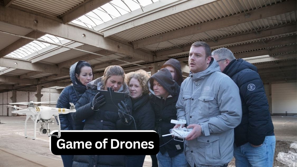 Billedet viser en gruppe kolleger samlet omkring en skærm og fjernbetjening, mens de styrer en drone i en stor indendørs hal. Aktiviteten hedder Game of Drones og er en innovativ teambuildingøvelse, hvor deltagerne skal samarbejde om at navigere og løse opgaver med droner – en spændende kombination af teknologi, strategi og teamwork.